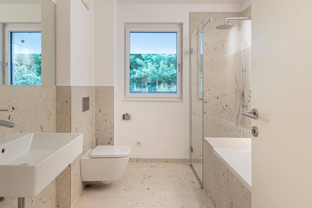Modernes Badezimmer mit beigefarbenen Fliesen, bodengleicher Dusche und Fenster.
