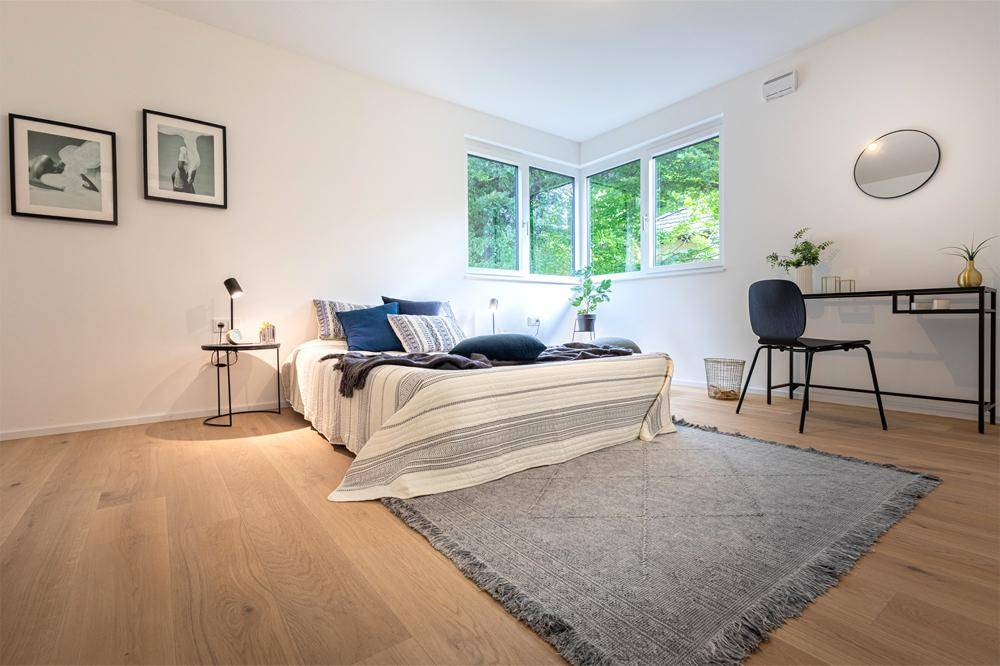 Helles Schlafzimmer mit Holzboden, Eckfenstern und Blick auf die Natur.