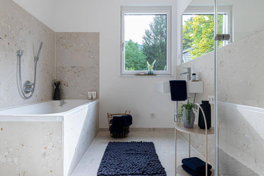 Modernes Badezimmer mit Badewanne, Dusche, Fenster und hellen Fliesen.
