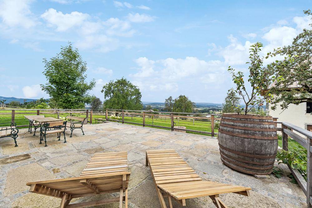 Gemütliche Steinterrasse mit Holzliegen und einem Fass als Dekoration, bietet einen weiten Blick in die Landschaft.
