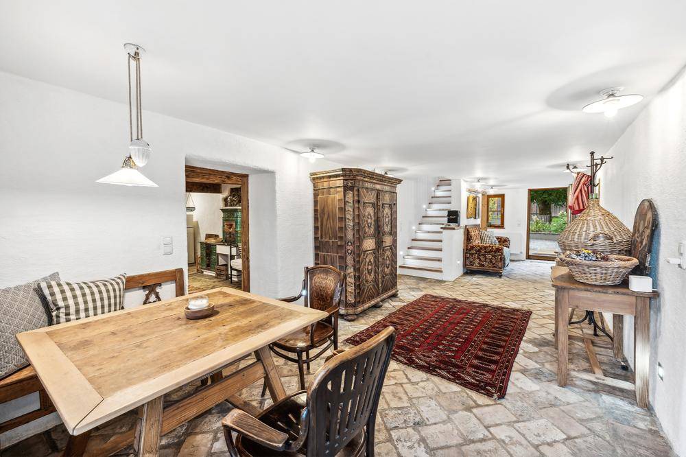 Rustikaler Wohn- und Essbereich mit Steinboden, Holztisch und einem traditionellen Kachelofen als Blickfang.