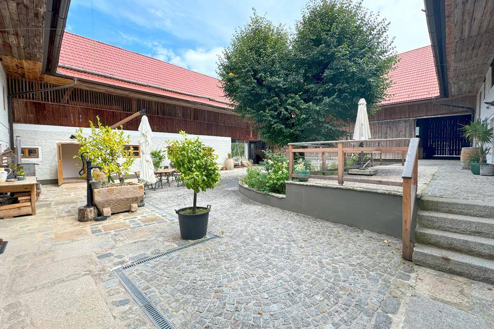 Idyllischer Innenhof mit Kopfsteinpflaster, Sitzgelegenheiten und grünen Pflanzen, umgeben von Gebäuden.