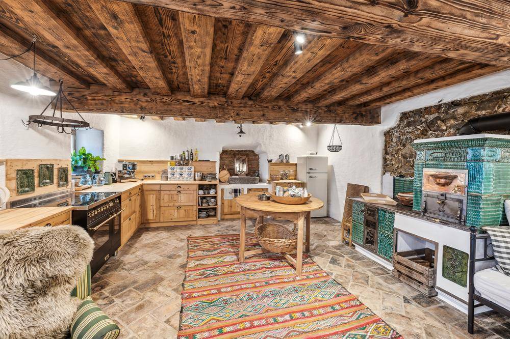 Rustikale Küche mit Holzbalkendecke, Steinwand und einem traditionellen Kachelofen, der Wärme spendet.