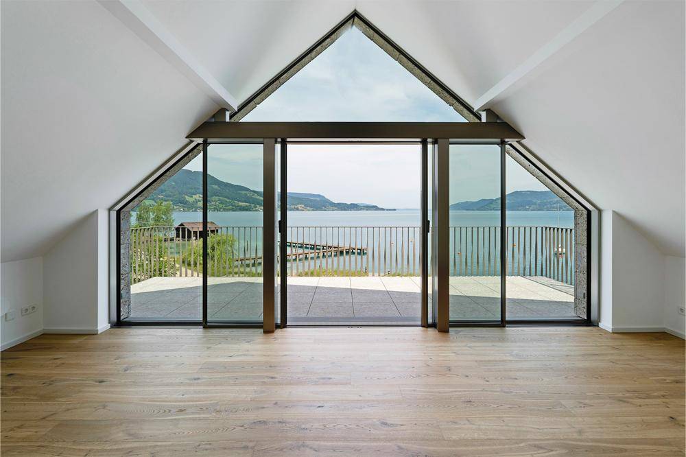 Heller Wohnraum mit hohen Decken, großen Fenstern und atemberaubendem Blick auf den See und die Berge.