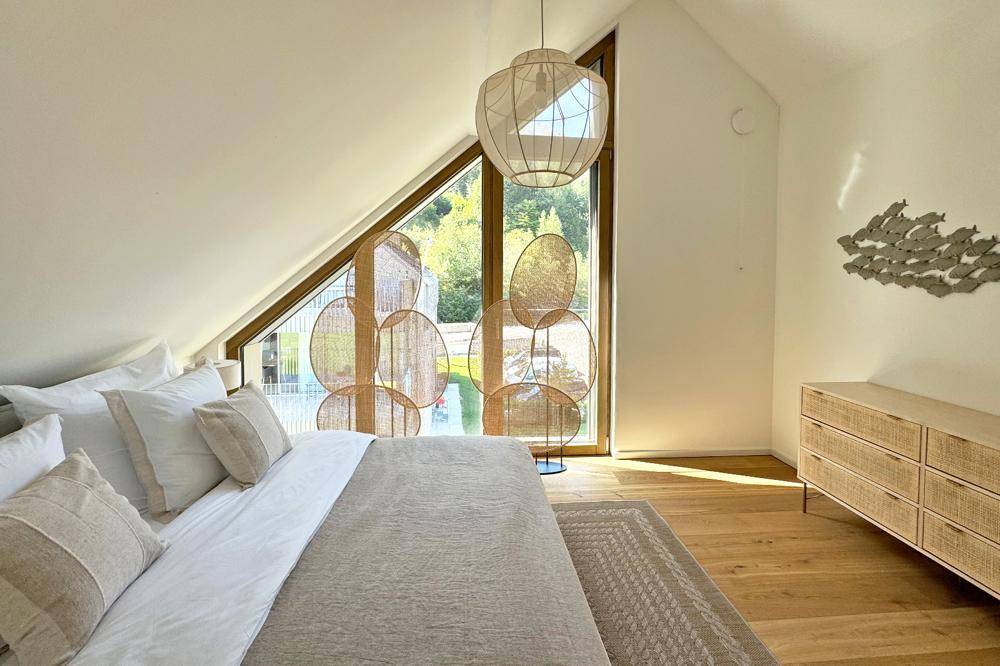 Modernes Schlafzimmer mit schrägen Decken, großen Fenstern und stilvoller Einrichtung.