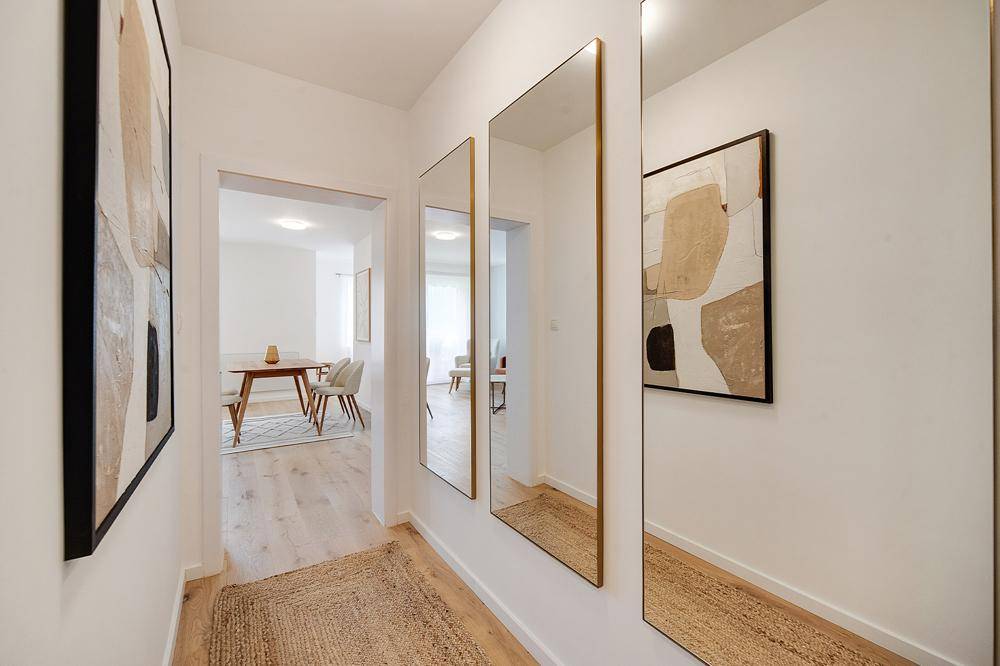 Heller Flur mit Holzfußboden, modernen Spiegeln und abstrakter Kunst an der Wand.