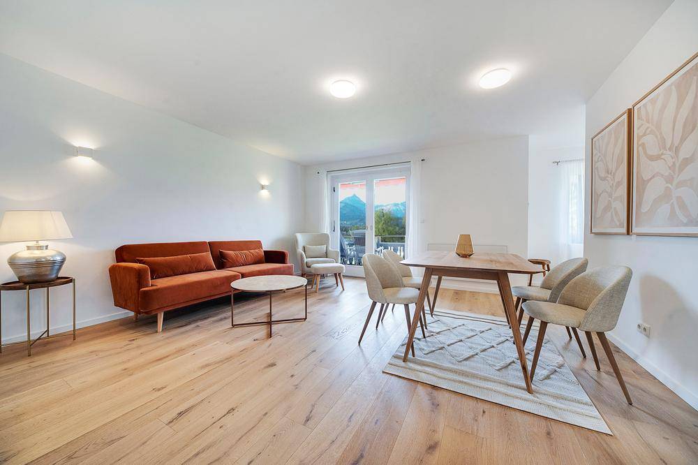 Geräumiger Wohn-Essbereich mit modernem Sofa, Esstisch und Zugang zum Balkon mit Bergblick.