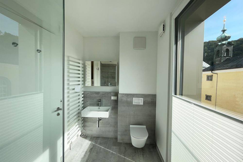 Modernes Badezimmer mit Waschbecken, wandhängendem WC, Handtuchheizkörper und Fensterblick.