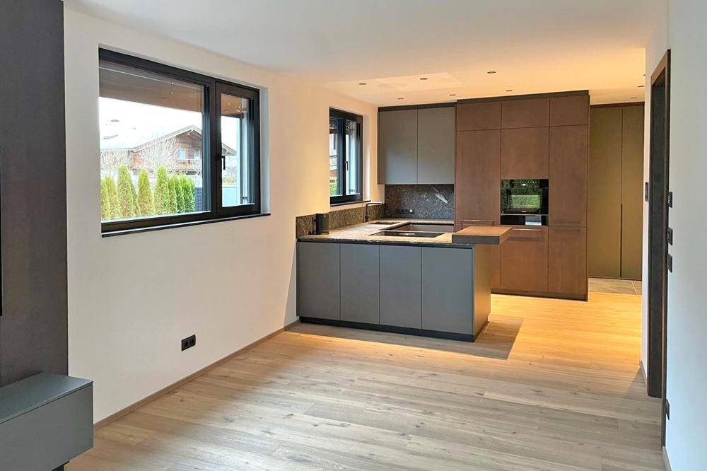 Moderne Küche mit dunklen Schränken, Holzboden und Blick ins Grüne.