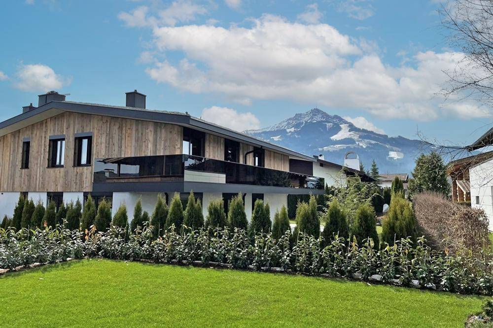 Moderne Villa mit Holzfassade und atemberaubendem Bergblick unter blauem Himmel.