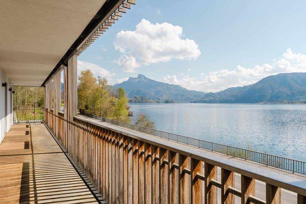 Langer Balkon mit Holzgeländer und atemberaubendem Panoramablick auf den See und die Berge.