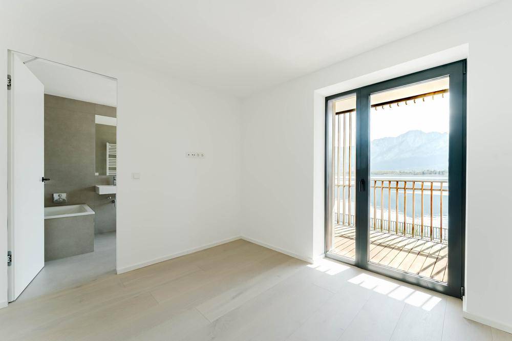 Helles Schlafzimmer mit Holzboden und Balkonzugang, bietet einen schönen Blick auf den See.