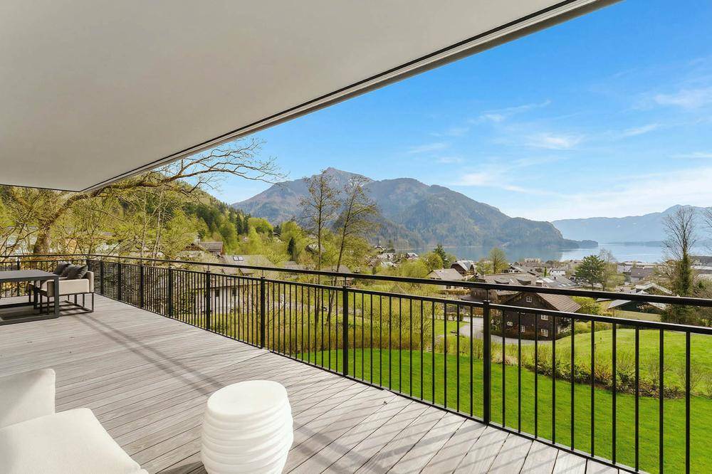 Geräumiger Balkon mit Holzdeck, Sitzgelegenheiten und spektakulärem Blick auf den See und die Berge.