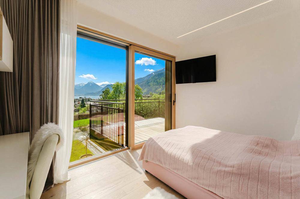 Helles Schlafzimmer mit großen Schiebetüren, Holzboden und direktem Zugang zum Balkon mit Seeblick.