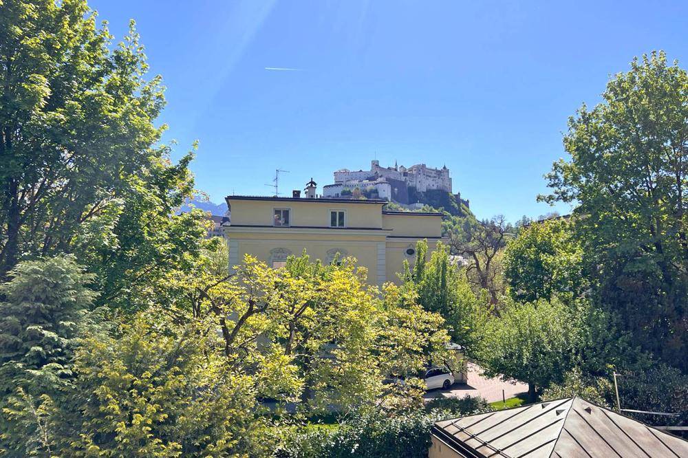 Panoramablick auf die Festung Hohensalzburg, umgeben von üppigem Grün und blauem Himmel.
