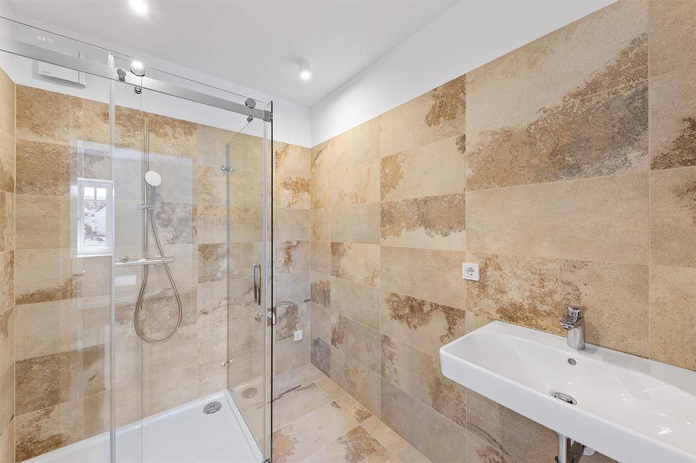 Modernes Badezimmer mit beigefarbenen Fliesen, begehbarer Dusche und Fenster.