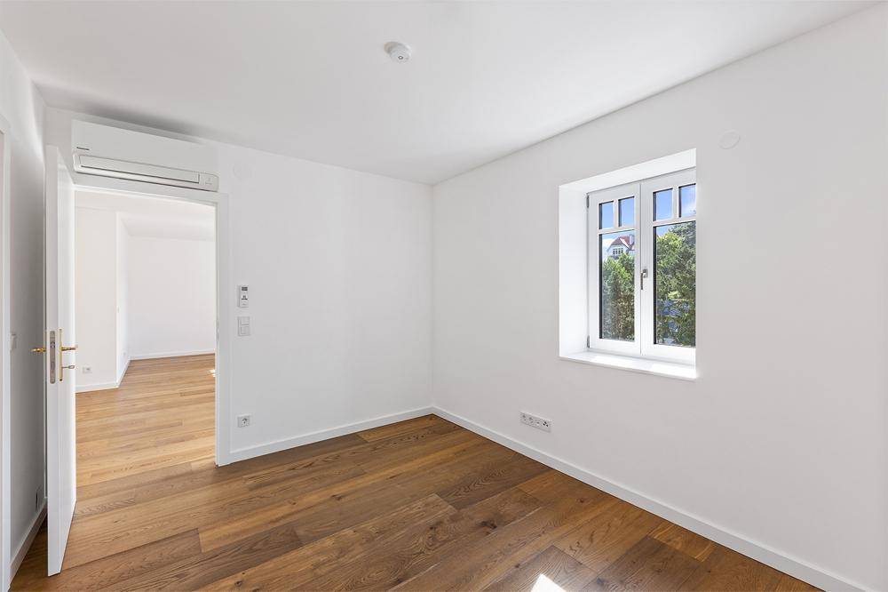 Helles Schlafzimmer mit Holzboden, Fenster und installierter Klimaanlage.