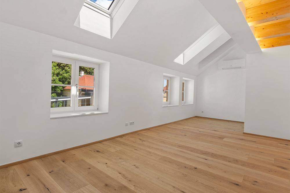 Helles Zimmer mit Holzboden, Dachfenstern und traditionellen Fenstern, ideal als Schlaf- oder Arbeitszimmer.