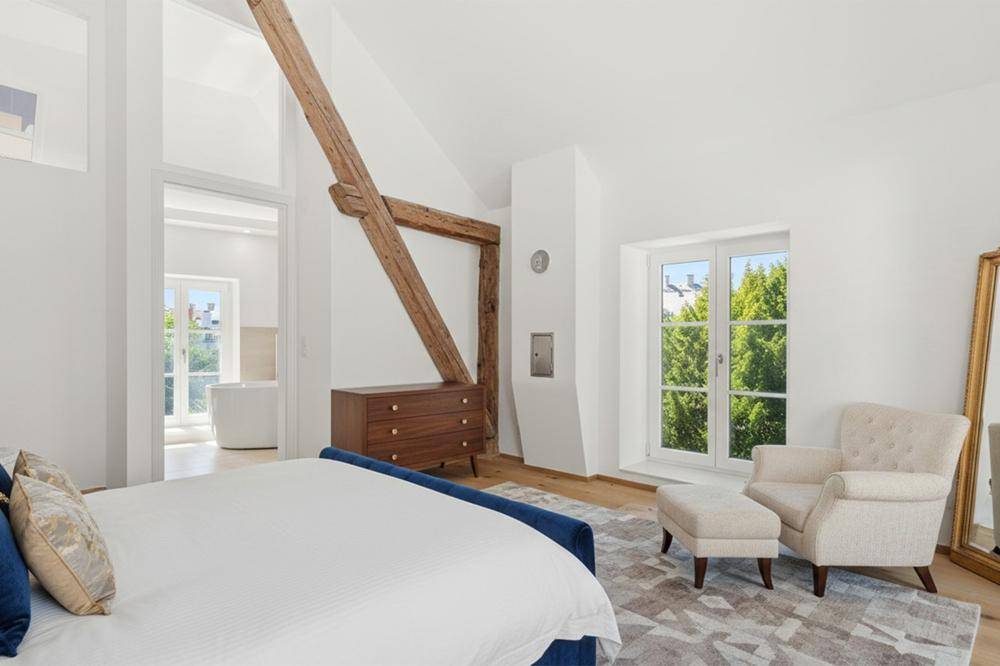 Gemütliches Schlafzimmer mit Holzboden, großem Fenster, bequemen Möbeln und einem rustikalen Holzbalken.