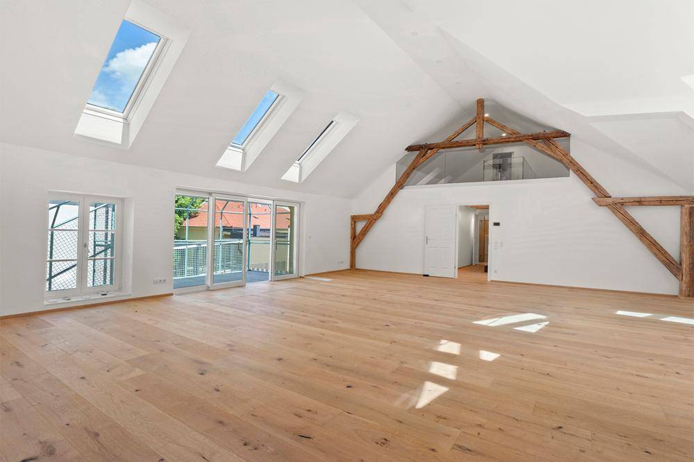 Geräumiger Wohnbereich mit Holzbalken, Dachfenstern und Zugang zu einem Balkon, bietet viel natürliches Licht.
