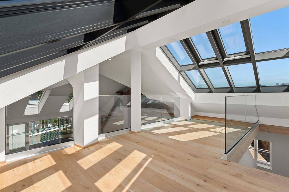 Heller Galeriebereich mit Glasgeländer, großen Dachfenstern und Holzboden, bietet einen offenen Blick.