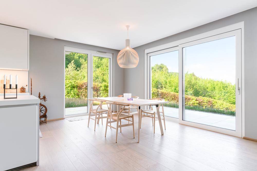 Lichtdurchfluteter Essbereich mit Holztisch, modernen Stühlen und Zugang zur Terrasse mit Grünblick.