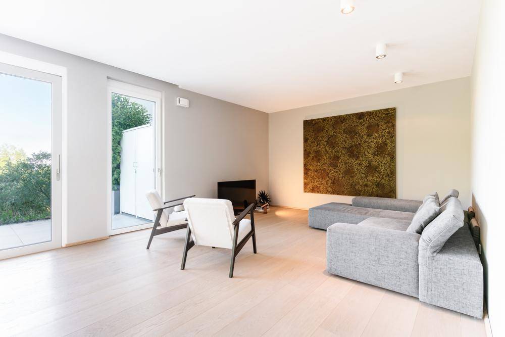 Geräumiges Wohnzimmer mit modernem Sofa, hellen Sesseln und großen Fenstern zum Außenbereich.