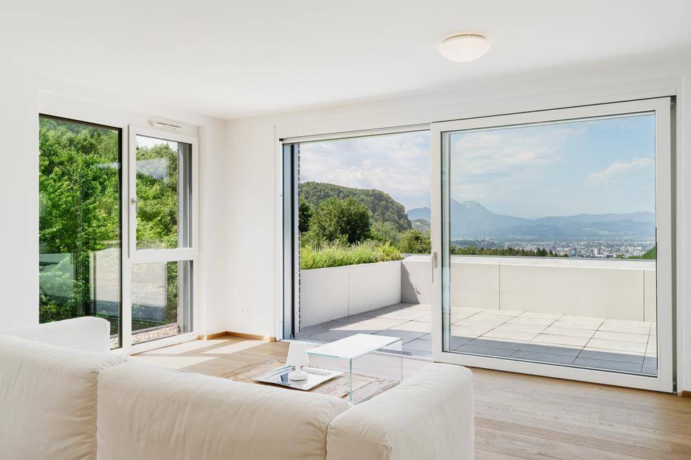 Helles Wohnzimmer mit großen Schiebetüren, die zu einer Terrasse mit Stadt- und Bergblick führen.