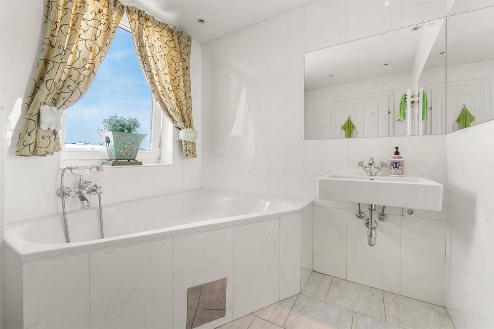 Helles Badezimmer mit Badewanne, wandmontiertem Waschbecken und Fenster für Tageslicht.