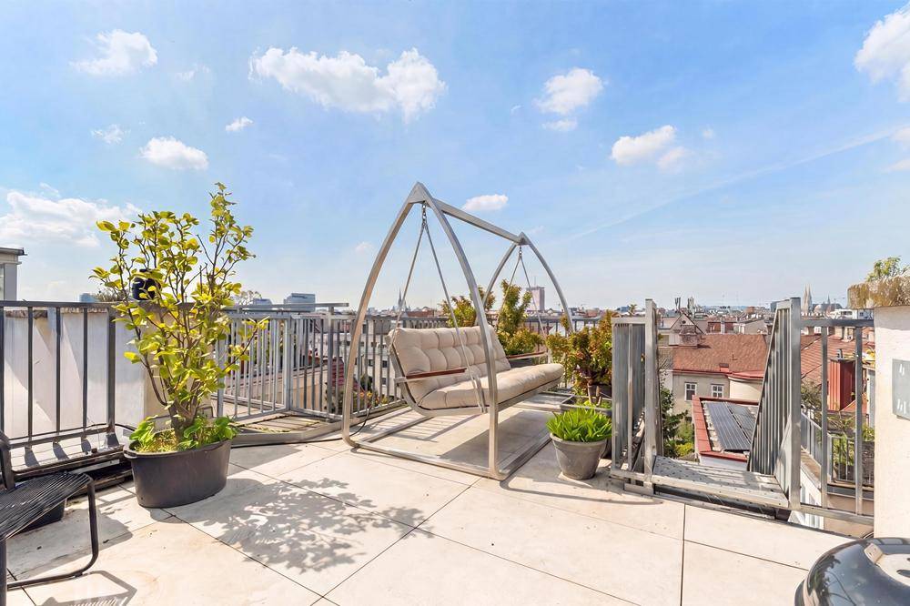 Sonnige Dachterrasse mit Schaukelbank, Pflanzen und weitem Panoramablick über die Stadt.