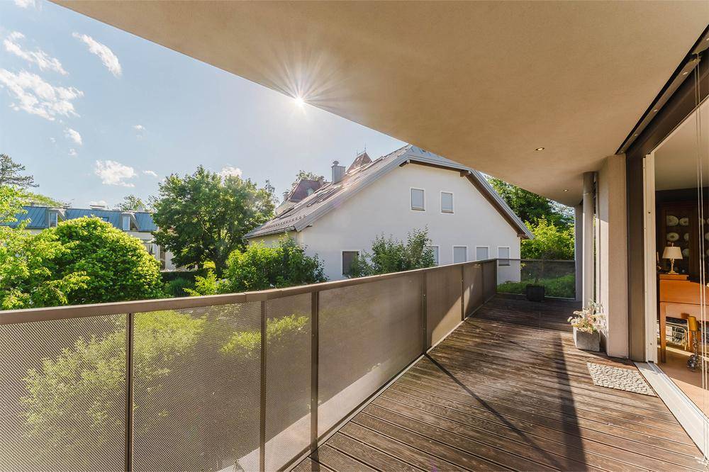 Breiter Balkon mit Holzdielen und freiem Blick auf die umliegende Wohnbebauung und Natur.