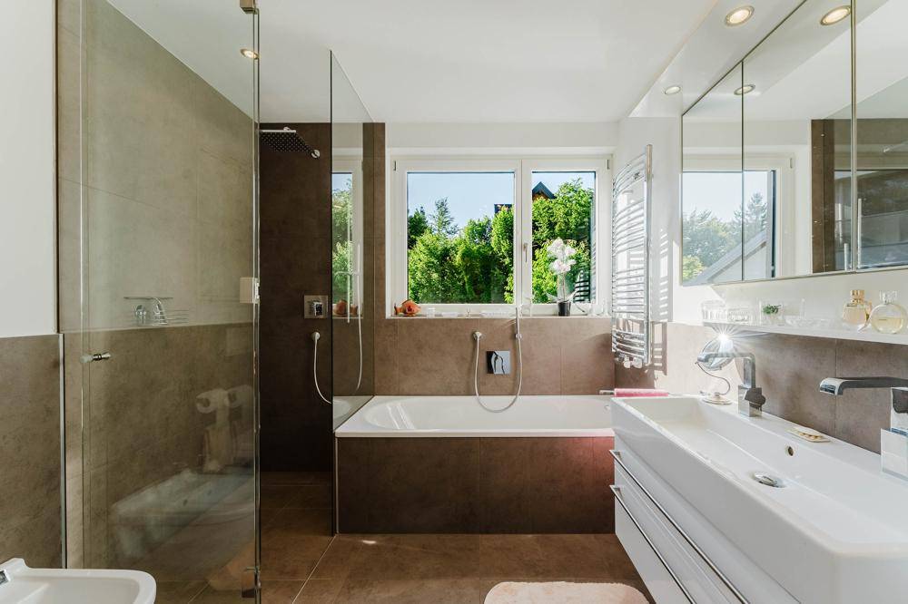 Modernes Badezimmer mit begehbarer Dusche, Badewanne und Fenster mit Blick ins Grüne.