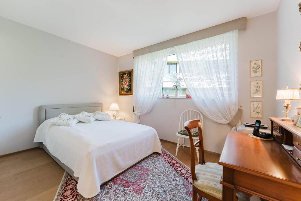 Helles Schlafzimmer mit Doppelbett, Schreibtisch und Fenster mit Vorhängen.