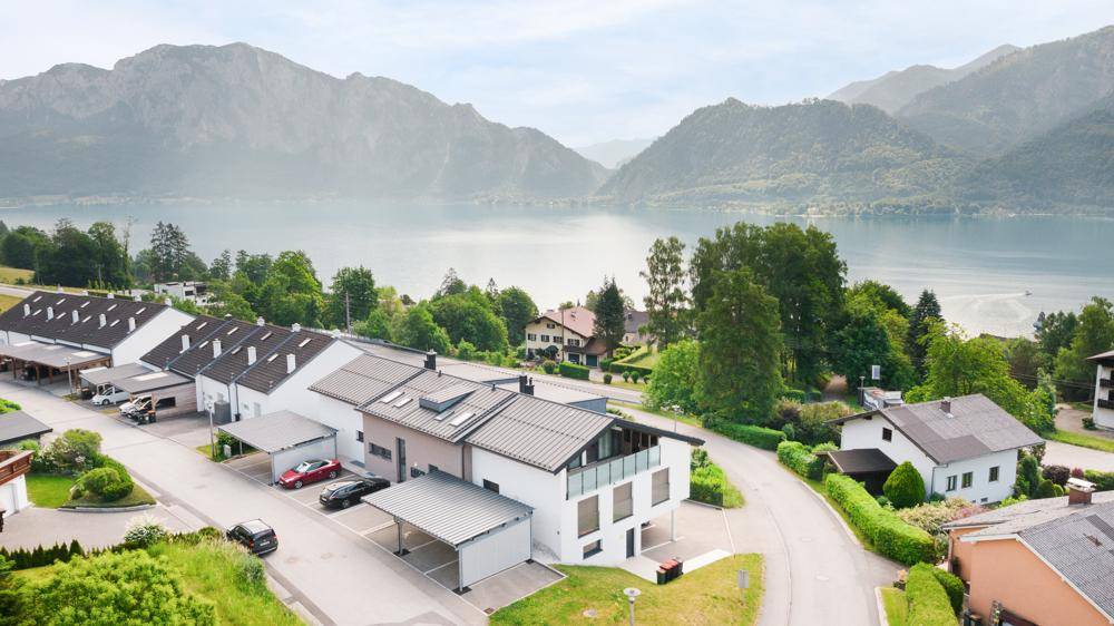 Luftaufnahme einer Wohnsiedlung am Seeufer mit modernen Häusern, Carports und Bergblick.