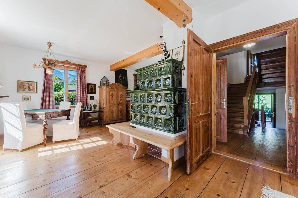 Geräumiger Wohn-Essbereich mit grünem Kachelofen, Holzboden und Zugang zur Treppe.