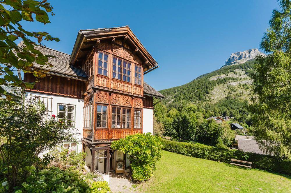 Charmantes Landhaus mit Holzbalkonen und Bergblick in sonniger Umgebung.