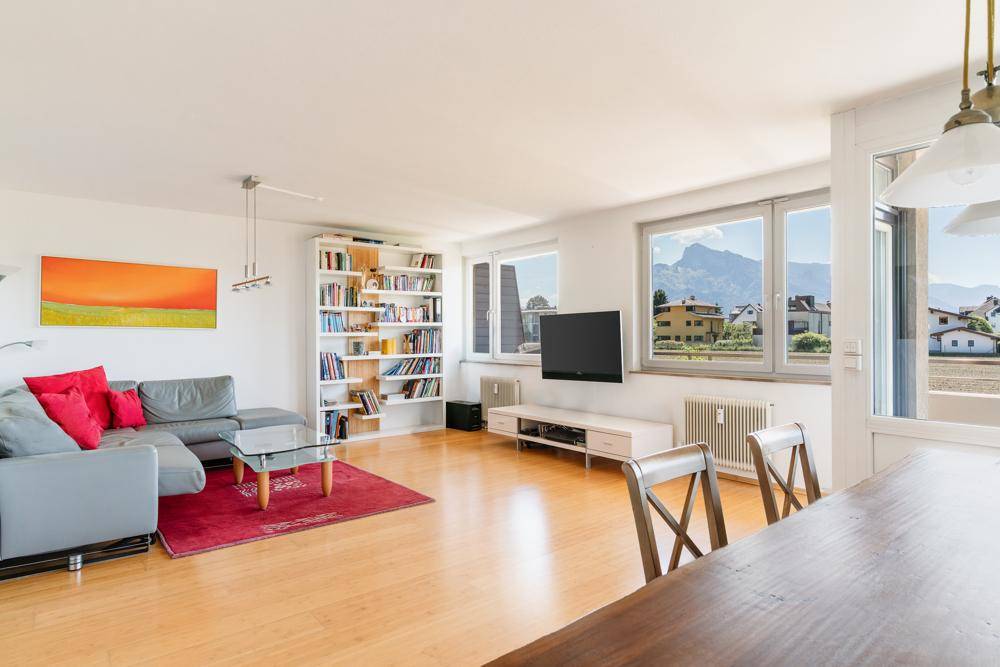Helles Wohnzimmer mit Parkettboden, gemütlicher Sitzecke und Bergblick durch große Fenster.
