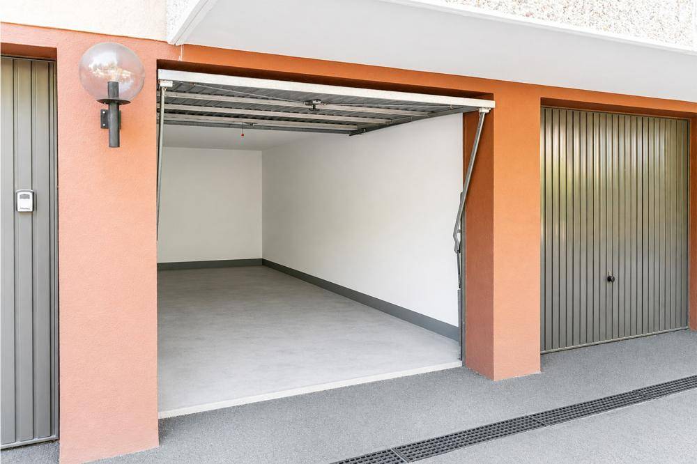 Leere Garage mit offenem Tor, sauberem Betonboden und Platz für ein Fahrzeug.