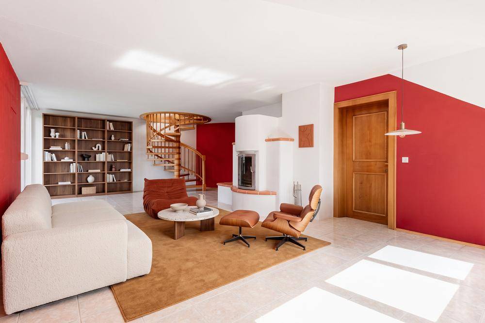 Geräumiges Wohnzimmer mit roten Wänden, Kamin, Wendeltreppe und stilvollen Möbeln.