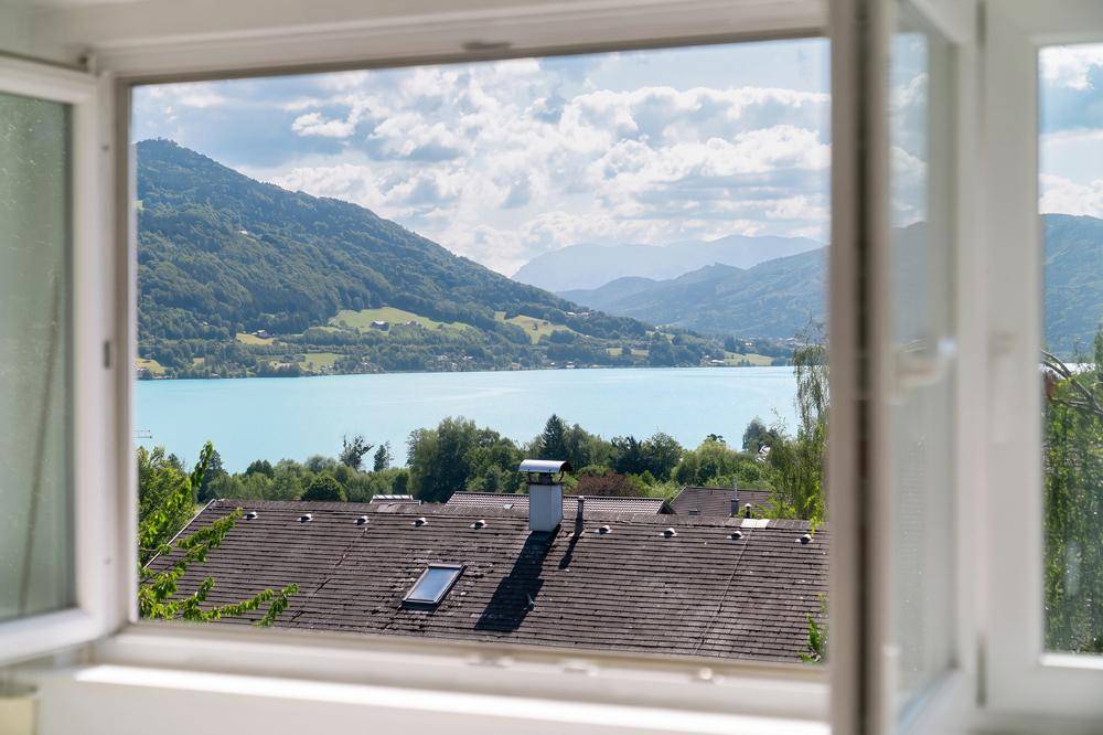 Panoramablick aus dem Fenster auf den malerischen See und die umliegenden Berge.
