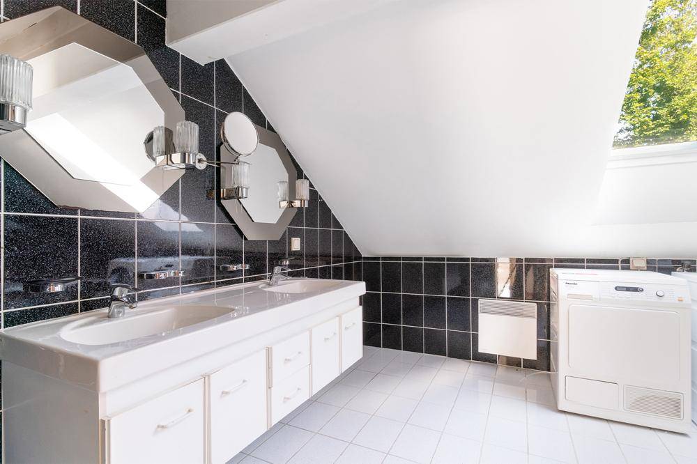 Badezimmer mit schwarz-weißen Fliesen, Doppelwaschbecken und Waschmaschine unter Dachschräge.