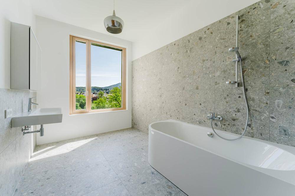 Modernes Badezimmer mit freistehender Badewanne, großer Fensterfront und hellen Fliesen.