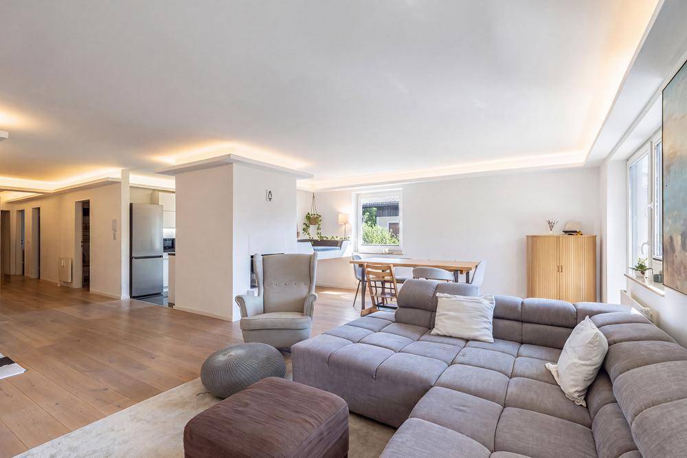Offener Wohn- und Essbereich mit großem Sofa, Holzboden und Blick in die Küche.