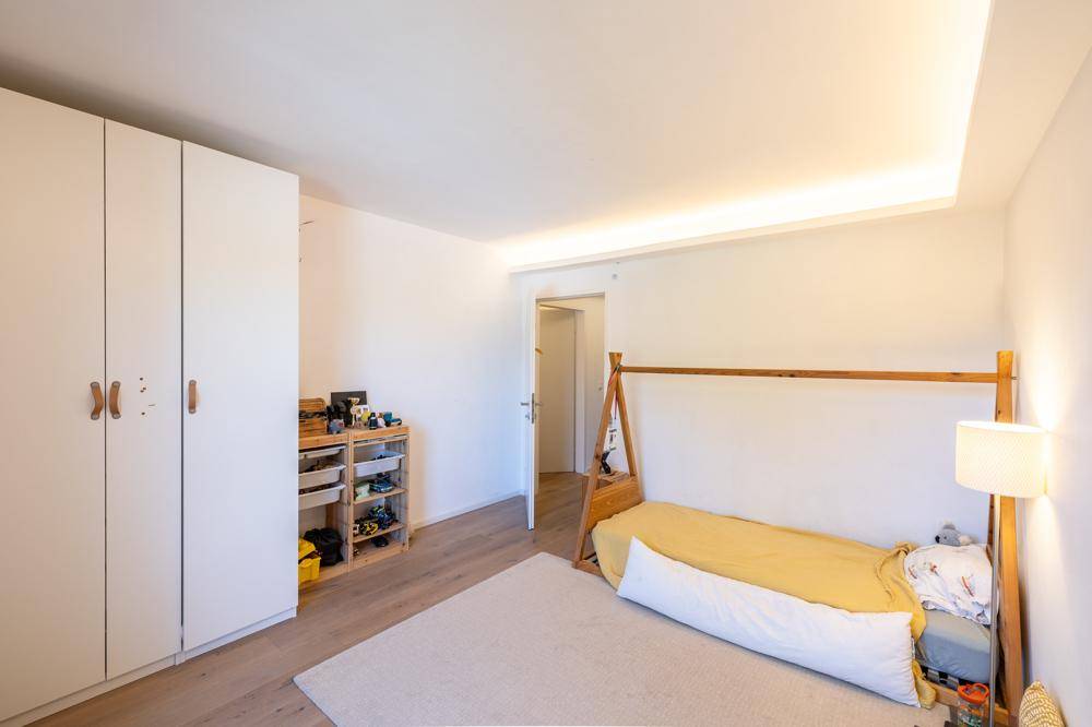 Helles Schlafzimmer mit Holzboden, weißem Kleiderschrank und minimalistischem Bettgestell.
