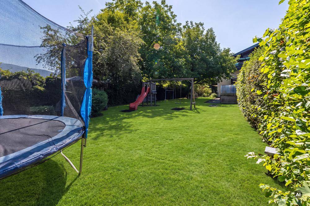 Großer grüner Garten mit Rasenfläche, Trampolin und Spielgeräten für Kinder.