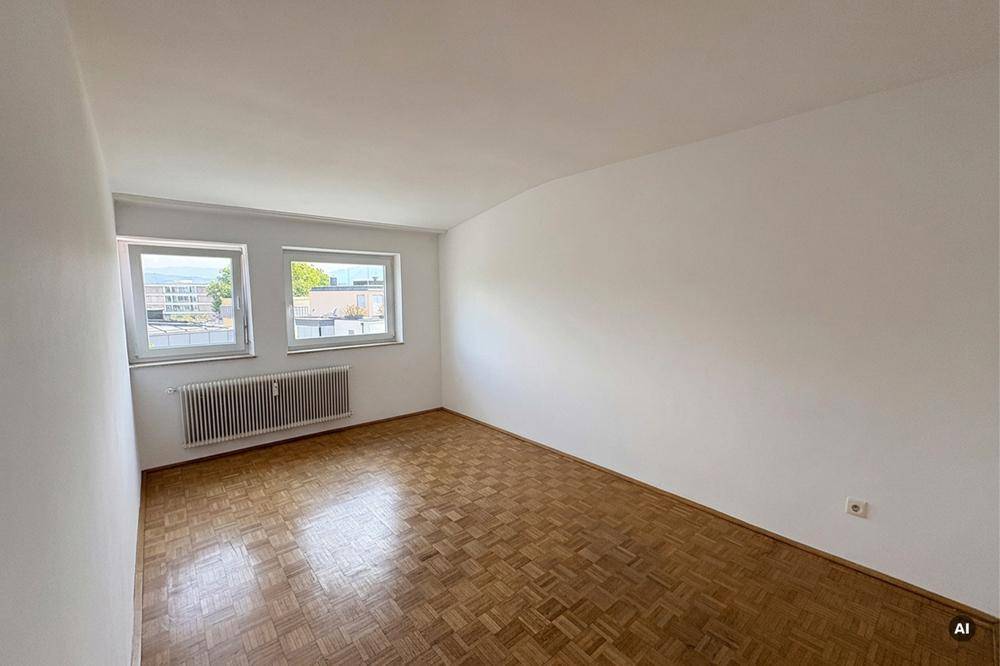 Leeres, helles Zimmer mit Parkettboden, weißen Wänden und zwei Fenstern.