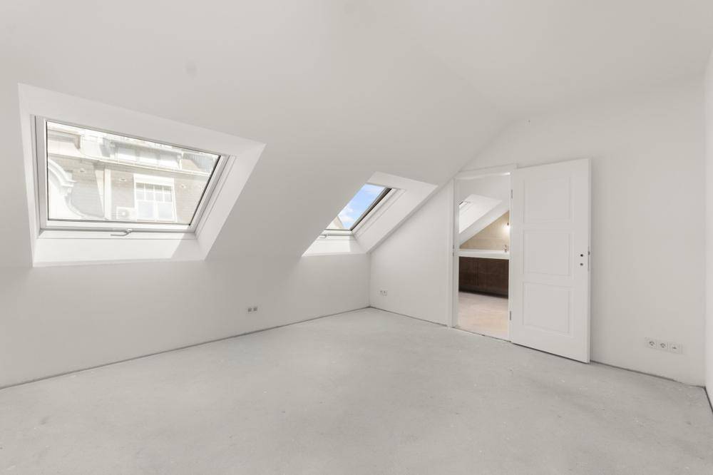 Geräumiger, leerer Raum im Dachgeschoss mit Dachfenstern und Zugang zu einem weiteren Zimmer.