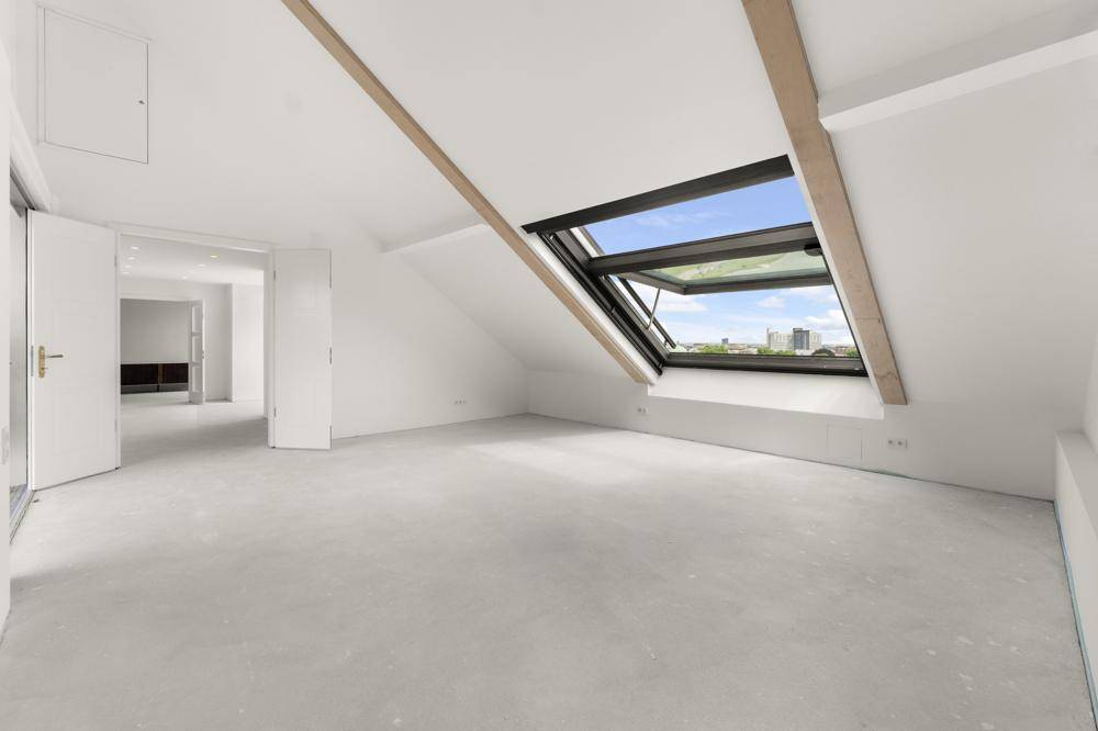 Heller, leerer Raum im Dachgeschoss mit großem Dachfenster und Blick in den Himmel.