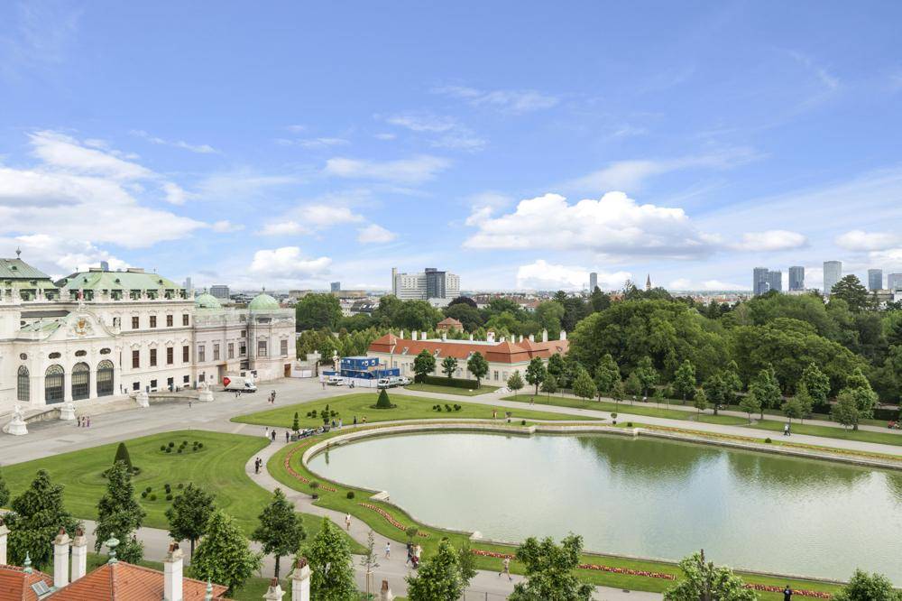 Panoramablick auf das Schloss Belvedere mit Teich, Parkanlage und der Wiener Skyline im Hintergrund.