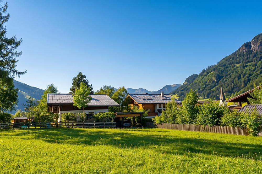 Ländliche Häuser mit Carports in einem sonnigen Tal, umgeben von bewaldeten Bergen.